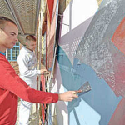 Bevor das Kunstwerk an der Fassade über dem Tufa-Haupteingang aufgefrischt wird, entfernen die Maler-Azubis Philipp Schmidt und Kevin Zimmermann verwitterte Farbschichten.