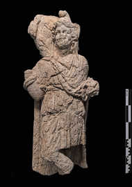 Eine aus Stein gehauene menschliche Figur, die einen Umhang und eine Mütze trägt