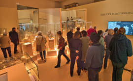Besucherinnen und Beswucher sehen sich Vitrinen in einem Ausstellungsraum an.