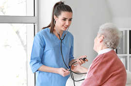 Eine junge Frau prüft einer alten Frau den Blutdruck