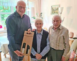 Dirk Steffens überreicht Herbert und Magdalena Selbach in deren Wohnung ein Weinpräsent.
