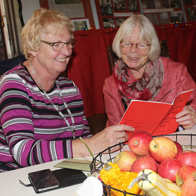 An einem herbstlich gedeckten Tisch informieren sich zwei Besucherinnen in der Programmbroschüre über die Angebote des Trierer Seniorenbüros. 