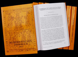 Mehrere Ausgaben des Kurtrierischen Jahrbuchs 2023 mit ockerfarbenem Einband, davon eines aufgeschlagen.