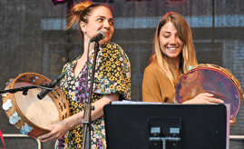 Zwei Musikerinnen mit Tamburinen stehen an einem Mikrofon