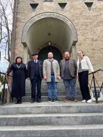 Fünf Personen stehen nebeneinander auf einer Treppe, die zum Eingang einer Synagoge führt. 