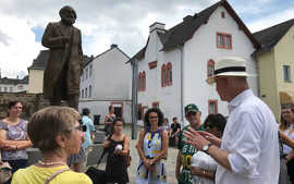 OB Wolfram Leibe versammelt die Teilnehmerinnen und Teilnehmer der Neubürgerführung um Triers neue Sehenswürdigkeit: die Karl-Marx-Statue auf dem Simeonstiftplatz. 
