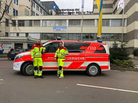 Mitarbeitende des Rettungsdienstes der Trierer Feuerwehr präsentieren die neue neongelbe Einsatzkleidung vor einem Notarzteinsatzfahrzeug.
