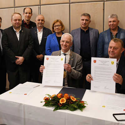 OB Wolfram Leibe und Isjums Bürgermeister Valerii Marchenko präsentieren die soeben unterzeichneten Partnerschaftsurkunden. Vertreterinnen und Vertreter des Trierer Stadtvorstands sowie der Stadträte von Trier und Isjum wohnten der Zeremonie bei.
