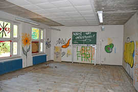Blick in ein ehemaliges Klassenzimmer. Die Wände sind voller Graffiti und ein Fenster wurde eingeworfen.