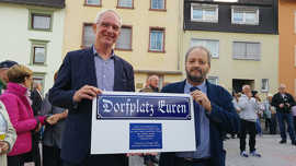 Ortsvorsteher Hans-Alwin Schmitz bedankt sich mit einem Schilder-Geschenk bei OB Leibe für die Unterstützung für den Dorfplatz.
