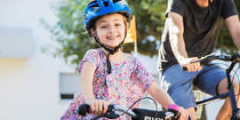 Ein lächelndes Kind mit blauem Fahrrad-Helm umgreift einen Fahrradlenker
