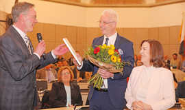 Im Großen Rathaussaal nimmt Oberbürgermeister Leibe lachend die eingerahmte Ernennungsurkunde von Innenminister Michael Ebling entgegen. In seiner Hand hält er bereits einen Blumenstrauß. Neben ihm steht Bürgermeisterin Elvira Garbes.