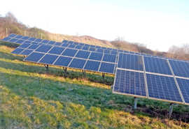 Solarmodule stehen in mehreren Reihen an einem Hang auf einer Wiese