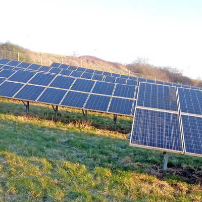 Solarmodule stehen in mehreren Reihen an einem Hang auf einer Wiese