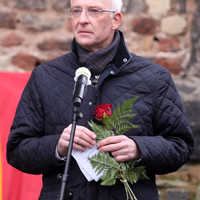 OB Wolfram Leibe hält eine rote Rose in der Hand und hält vor der Porta Nigra eine Rede.