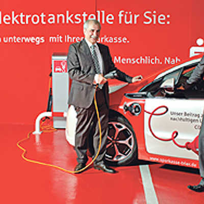 Vorstandsvorsitzender Remigius Kühnen (l.) stellt mit OB  Klaus Jensen das neue Hybrid-Fahrzeug der Sparkasse vor und nimmt es an der hauseigenen Elektro-Tankstelle in Betrieb.