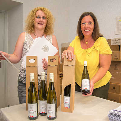 Monika Mischtian (links) und Erika Dahlem vom städtischen Protokollreferat präsentieren den neuen OB-Wein und die Urkunden, die ab dem 100. Geburtstag sowie bei Ehejubiläen überreicht werden.