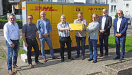 Dr. Johannes Weinand freut sich mit Bernd Dietrich sowie weiteren Beteiligten von der Post und dem SKV Trier über die neue Packstation in Heiligkreuz.