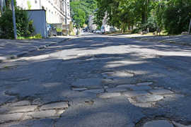 Blick auf die stark beschädigte Agritiusstraße mit zahlreichen Schlaglöchern und Flickstellen. Die Straße gehört zu den für dieses Jahr geplanten Sanierungsprojekten der Stadt. 