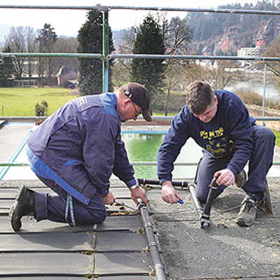 Vor dem Aufbringen der neuen Dacheindeckung entfernen Michael Föhr und Jörg Schwarz (v. l.) vom Nordbad-Team Absorbermatten und Wasserleitungen der Solaranlage, die später wieder installiert werden.