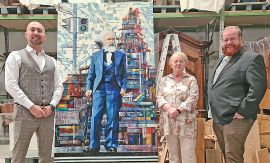 Drei Personen stehn neben einem zwei Meter hohen Gemälde, das Marx vor einem Berg Bücher zeigt