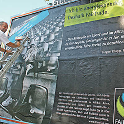 Oberbürgermeister Klaus Jensen bringt zum Auftakt der  Fairtrade-Botschafterkampagne den Aufkleber „Wir sind Fairtrade-Town“ auf dem Plakat im Martinerfeld an.