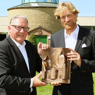 arry Thiele, Vorstandsvorsitzender der Kulturstiftung (links), übergibt die Stifterplatte an Jan Niewodniczanski von der Bitburger Braugruppe. Foto: Agenturhaus