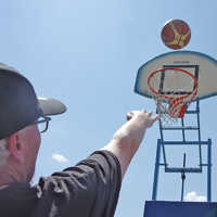 Ein Man mit Schirmmütze wirft einen Ball auf einen Basketballkorb.