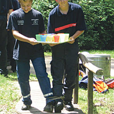 Bei einem Geschicklichkeitsspiel werden zwei Feuerwehrmänner mit einem Band am Bein zusammengebunden und müssen ein Tablett mit Wassergläsern innerhalb von drei Minuten durch einen Hindernisparcours bringen.  Foto: Feuerwehr