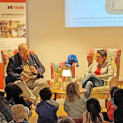 Kulturdezernent Markus Nöhl liest den zahlreichen Kindern aus Axel Schefflers Buch „Riese Rick macht sich schick“ vor. Auch Büchereileiterin Andrea May hört gespannt zu. Foto: Stadtbücherei