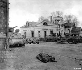 historisches Foto zeigt Militärfahrzeuge auf einer Straße, im Vordergrund liegt eine abgedeckte Leiche
