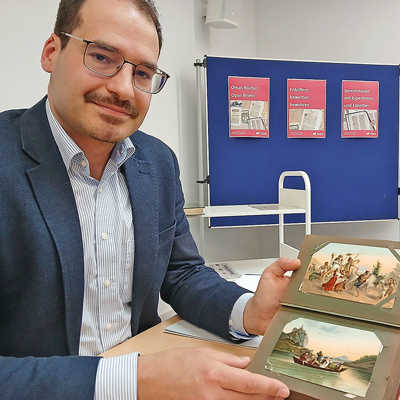 Archivar Jort Blazejewski begutachtet eine Sammlung kolorierter Postkarten aus dem frühen 20. Jahrhundert.