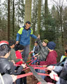 Im Weisshauswald befestigen die Erlebnispädagogen ein langes Gurtband an einem Baum, das die Jugendlichen gemeinsam straffhalten, so dass eine Person darüber laufen kann. 