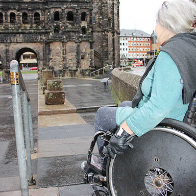 Heike Unterrainer mit ihrem Rollstuhl vor der zu steilen Rampe an der Porta, an die sich ein Sockel (Bildmitte) anschließt. Jetzt ist Besserung in Sicht.