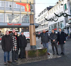 Gruppenbild von sieben Personen in Winterjacken am Pranger in der Grabenstraße