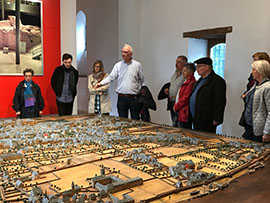 OB Wolfram Leibe (4. v. l.) erklärt 13 neu nach Trier gezogenen Bürgerinnen und Bürgern das historische Stadtbild an einem Modell im Stadtmuseum.