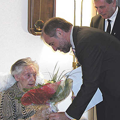 Mit einem Blumenstrauß in den Stadtfarben Gelb und Rot gratuliert OB Klaus Jensen Margarete Kollmann zu ihrem 102. Geburtstag. Rechts ihr Sohn, Pfarrer Klaus Kollmann.