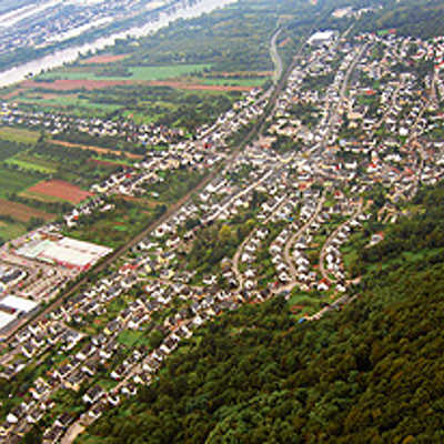 Blick auf die langgestreckte Siedlungsstruktur des Stadtteils Zewen zwischen der Mosel und dem Waldgebiet. Im Tal verlaufen unter anderem die Hauptverkehrsachse B 49 sowie die Bahnstrecke