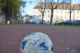 Ein Fußball liegt auf dem Bolzplatz, im Hintergrund ist das Rathaus.