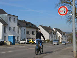 Fahrradfahrer von hinten mit neuem Schild am Straßenrand