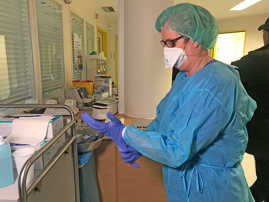 Eine Pflegerin zieht sich im Corona-Gemeinschaftskrankenhaus blaue Schutzkleidung über.