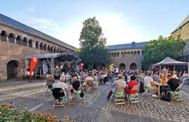 Konzertbesucher sitzen an Tischen vor einer Bühne vor der historischen Kulisse des Brunnenhofs 