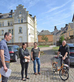 Thilo Becker, Marc Borkam, Larissa Bläser-Stangier und Susanne Nipp stehen in einem Wohngebiet mit älteren Gebäuden auf einer Straße mit Kopfsteinpflaster und unterhalten sich.