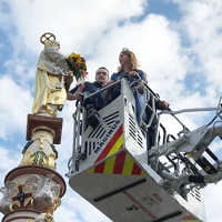 Weinkönigin Bärbel Ellwanger und Oberbürgermeister Wolfram Leibe (verdeckt) legen in Begleitung eines Feuerwehrmanns der Petrusfigur auf dem Hauptmarkt per Drehleiter Blumen in den Arm.