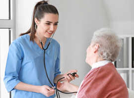 Eine ältere Frau im Gesprächemit einer jugen Pflegerin, die ein Stethoskop hält.