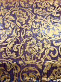 Nahaufnahme eines Bucheinbands mit goldenen Ornamenten auf violettem Hintergrund