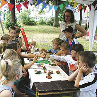 Mit Betreuerin Kerstin Schorer-Hach von der mobilen Spielaktion (hinten rechts) gestalten die Kinder aus Trier-West aus Knete oder Kork Gerätemodelle für ihren Spielplatz.