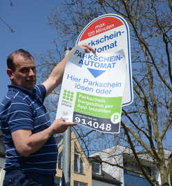 Peter Ogrodnik von der Firma Wöffler überklebt ein Hinweisschild mit einem Hinweis zum Handyparken