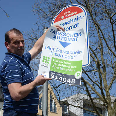 Peter Ogrodnik von der Firma Wöffler überklebt ein Hinweisschild mit einem Hinweis zum Handyparken