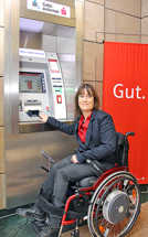 Eine Rollstuhlfahrerin bedient einen der umgerüsteten Geldautomaten. Foto: Sparkasse